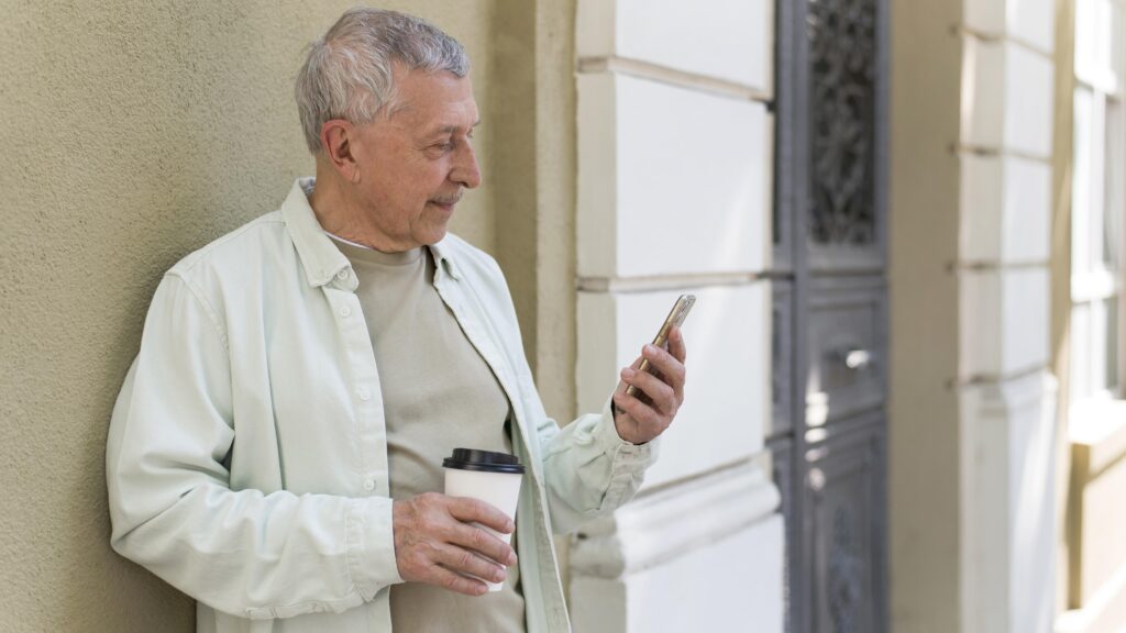 oudere man drinkt koffie en kijkt op 50+ mobiel